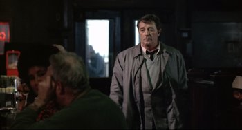 Movie still from “The Friends of Eddie Coyle” (1973), directed by Peter Yates – A man in a suit and tie standing in front of another man; Medium shot, Over the shoulder angle