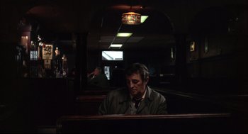 Movie still from “The Friends of Eddie Coyle” (1973), directed by Peter Yates – A man sitting at a table in front of a clock; Medium shot, Over the shoulder angle