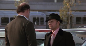 Movie still from “The Friends of Eddie Coyle” (1973), directed by Peter Yates – A man in a suit and a hat talking to another man in a suit; Medium shot, Over the shoulder angle