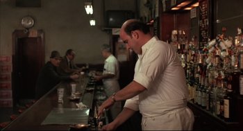 Movie still from “The Friends of Eddie Coyle” (1973), directed by Peter Yates – A man standing at a counter preparing food; Wide shot, Over the shoulder angle