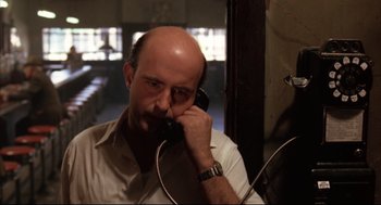 Movie still from “The Friends of Eddie Coyle” (1973), directed by Peter Yates – A man with a bald head talking on a phone; Close Up shot, Low angle