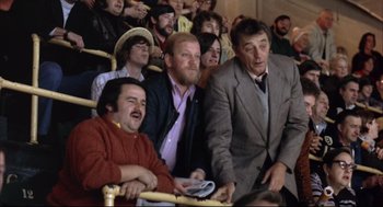 Movie still from “The Friends of Eddie Coyle” (1973), directed by Peter Yates – A group of men sitting next to each other in front of a crowd; Medium shot, High angle