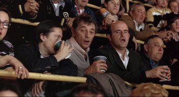 Movie still from “The Friends of Eddie Coyle” (1973), directed by Peter Yates – A group of men sitting in a stadium holding cups; Medium shot, High angle