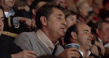 Movie still from “The Friends of Eddie Coyle” (1973), directed by Peter Yates – A group of men sitting in a stadium holding cups; Close Up shot, Low angle