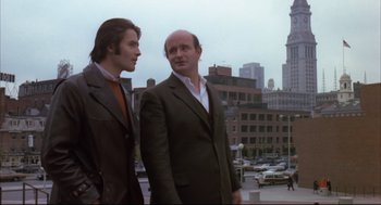 Movie still from “The Friends of Eddie Coyle” (1973), directed by Peter Yates – Two men standing next to each other on a city street; Medium shot, Low angle