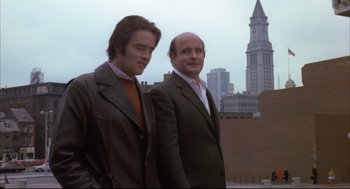 Movie still from “The Friends of Eddie Coyle” (1973), directed by Peter Yates – A couple of men standing next to each other on top of a building; Medium shot, Low angle