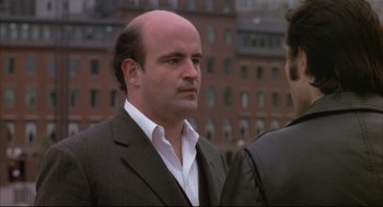 Movie still from “The Friends of Eddie Coyle” (1973), directed by Peter Yates – A man in a suit and tie standing next to another man in a suit; Close Up shot, Over the shoulder angle