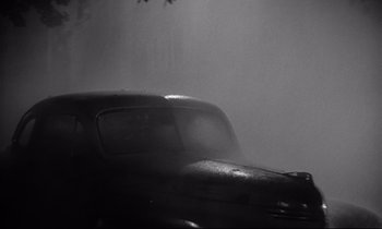 Movie still from “The Fugitive Kind” (1960), directed by Sidney Lumet – A black and white photo of a car in the rain; Wide shot, Low angle
