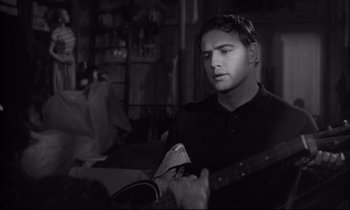 Movie still from “The Fugitive Kind” (1960), directed by Sidney Lumet – A man holding a guitar in a room with other people; Close Up shot, Over the shoulder angle