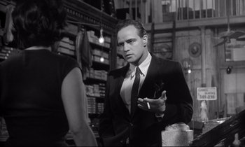 Movie still from “The Fugitive Kind” (1960), directed by Sidney Lumet – A black and white photo of a man smoking a cigarette; Medium shot, Over the shoulder angle