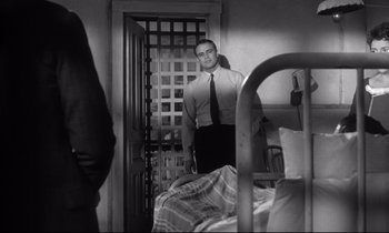 Movie still from “The Fugitive Kind” (1960), directed by Sidney Lumet – A black and white photo of a man standing in front of a bed; Medium shot, Low angle
