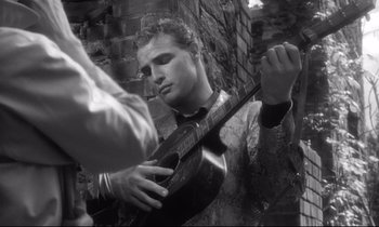 Movie still from “The Fugitive Kind” (1960), directed by Sidney Lumet – A man holding an instrument while standing next to a brick wall; Close Up shot, Low angle