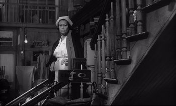 Movie still from “The Fugitive Kind” (1960), directed by Sidney Lumet – An older woman standing in front of a set of wooden stairs; Medium shot, Low angle
