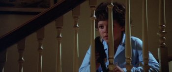 Movie still from “The Funhouse” (1981), directed by Tobe Hooper – A young boy holding a cell phone while standing on a staircase railing; Close Up shot, High angle