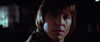 Movie still from “The Funhouse” (1981), directed by Tobe Hooper – A young man with long brown hair is looking at the camera; Close Up shot, Low angle