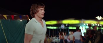 Movie still from “The Funhouse” (1981), directed by Tobe Hooper – A man in a white shirt is standing in front of a crowd; Medium shot, Over the shoulder angle