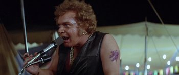 Movie still from “The Funhouse” (1981), directed by Tobe Hooper – A man in a leather vest singing into a microphone; Close Up shot, Low angle