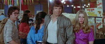 Movie still from “The Funhouse” (1981), directed by Tobe Hooper – A man in a brown jacket standing next to a woman in a blue dress; Medium shot, Over the shoulder angle