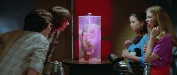 Movie still from “The Funhouse” (1981), directed by Tobe Hooper – Two people looking at a glass case with a fetus in it; Medium shot, High angle