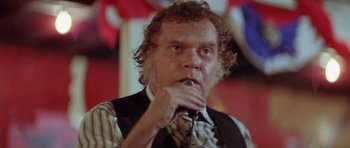 Movie still from “The Funhouse” (1981), directed by Tobe Hooper – A man with curly hair and a tie is sitting in front of a wall; Close Up shot, Low angle