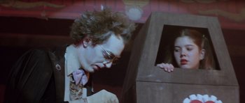 Movie still from “The Funhouse” (1981), directed by Tobe Hooper – A man with a bow tie is looking down at a box in front of him; Medium shot, Over the shoulder angle