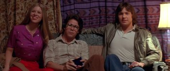 Movie still from “The Funhouse” (1981), directed by Tobe Hooper – A man and a woman sitting next to each other holding remotes; Medium shot, Low angle
