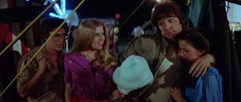Movie still from “The Funhouse” (1981), directed by Tobe Hooper – A man and a woman standing next to each other holding cotton candy; Medium shot, Over the shoulder angle