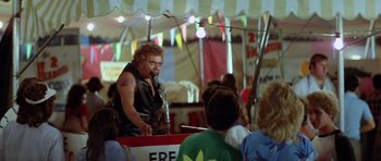 Movie still from “The Funhouse” (1981), directed by Tobe Hooper – A man in a black leather jacket standing in front of a crowd of onlookers; Medium shot, Over the shoulder angle