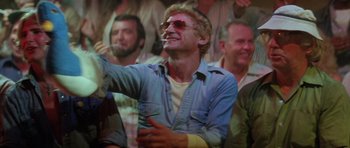 Movie still from “The Funhouse” (1981), directed by Tobe Hooper – A group of people watching a man smoking a cigarette; Medium shot, Over the shoulder angle