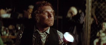 Movie still from “The Funhouse” (1981), directed by Tobe Hooper – A man holding a flashlight in a dark room; Close Up shot, Low angle