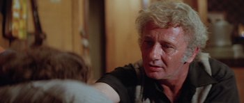 Movie still from “The Funhouse” (1981), directed by Tobe Hooper – An older man sitting in front of a wooden wall; Close Up shot, Over the shoulder angle