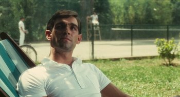 Movie still from “The Garden of the Finzi-Continis” (1970), directed by Vittorio De Sica – A man sitting in the grass with a tennis court in the background; Close Up shot, Over the shoulder angle