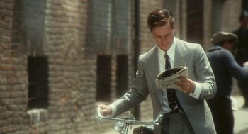 Movie still from “The Garden of the Finzi-Continis” (1970), directed by Vittorio De Sica – A man in a suit and tie standing next to a bike; Medium shot, Over the shoulder angle