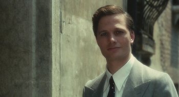 Movie still from “The Garden of the Finzi-Continis” (1970), directed by Vittorio De Sica – A man wearing a suit and tie standing in front of a wall; Close Up shot, Over the shoulder angle