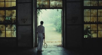 Movie still from “The Garden of the Finzi-Continis” (1970), directed by Vittorio De Sica – A man holding a tennis racquet standing in front of a door; Wide shot, Low angle