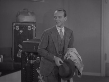 Movie still from “The Gay Divorcee” (1934), directed by Mark Sandrich – A man in a suit and tie holding a hat and smiling; Medium shot, High angle
