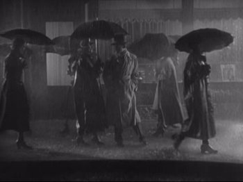 Movie still from “The Gay Divorcee” (1934), directed by Mark Sandrich – A black and white photo of a group of people walking in the rain; Wide shot, Low angle