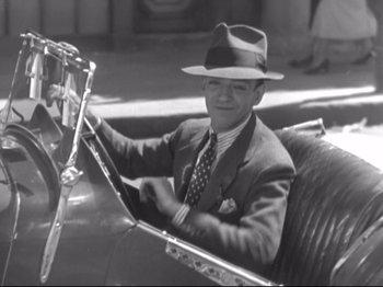 Movie still from “The Gay Divorcee” (1934), directed by Mark Sandrich – An old photo of a man in a suit driving a car; Medium shot, High angle