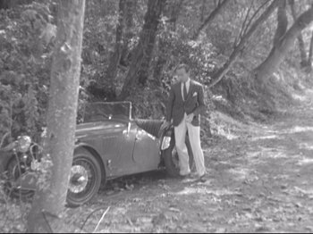 Movie still from “The Gay Divorcee” (1934), directed by Mark Sandrich – A man standing next to an old car in a wooded area; Wide shot, High angle