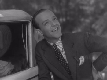 Movie still from “The Gay Divorcee” (1934), directed by Mark Sandrich – An old black and white photo of a man in a suit and tie next to a car; Medium shot, Low angle