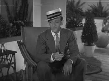 Movie still from “The Gay Divorcee” (1934), directed by Mark Sandrich – A man sitting in a chair wearing a suit and a hat; Medium shot, High angle