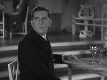 Movie still from “The Gay Divorcee” (1934), directed by Mark Sandrich – A man sitting at a table with a glass of wine; Medium shot, High angle