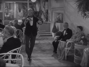 Movie still from “The Gay Divorcee” (1934), directed by Mark Sandrich – A man in a suit and bow tie is holding a violin; Wide shot, High angle