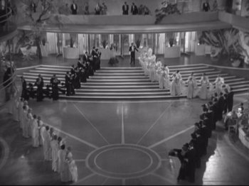 Movie still from “The Gay Divorcee” (1934), directed by Mark Sandrich – A black and white photo of a group of people standing in front of an audience; Extreme Wide shot, High angle