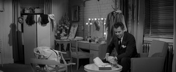 Movie still from “The Gazebo” (1959), directed by George Marshall – A black and white photo of a man cutting a cake; Wide shot, High angle