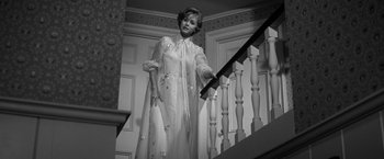 Movie still from “The Gazebo” (1959), directed by George Marshall – An old photo of a woman in a dress on a staircase; Medium shot, Low angle