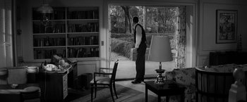 Movie still from “The Gazebo” (1959), directed by George Marshall – A black and white photo of a man standing in front of a window; Wide shot, Over the shoulder angle