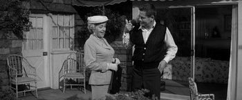 Movie still from “The Gazebo” (1959), directed by George Marshall – An older woman standing next to an older man in front of a building; Medium shot, Over the shoulder angle