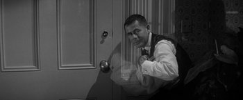 Movie still from “The Gazebo” (1959), directed by George Marshall – A black - and - white photo of a man leaning against a door; Medium shot, Over the shoulder angle