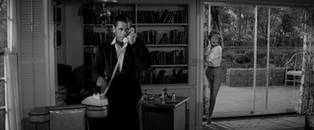 Movie still from “The Gazebo” (1959), directed by George Marshall – A man talking on a phone while a woman stands in front of him; Wide shot, Low angle